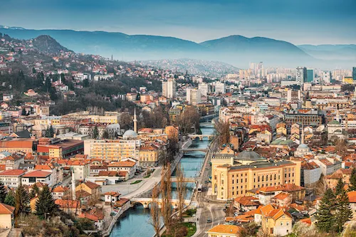 Bosnia and Herzegovina, Sarajevo - As evening descends, the city skyline glows with a warm hue against the backdrop of the Miljacka River