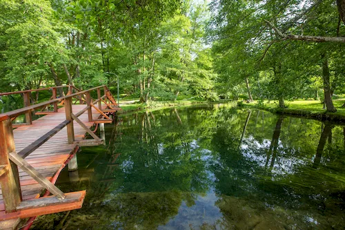 Bosnia and Herzegovina, Sarajevo - Wooden footbridge over the crystal clear river in Vrelo Bosne Nature Park